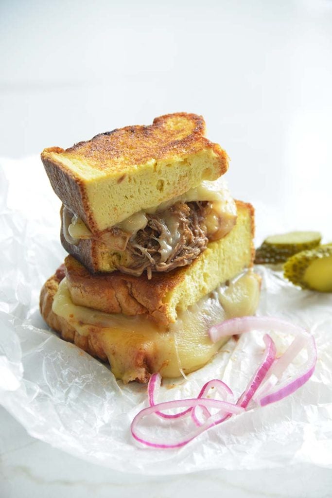 3 cheese keto grilled cheese sandwich on parchment paper with pickles and red onions