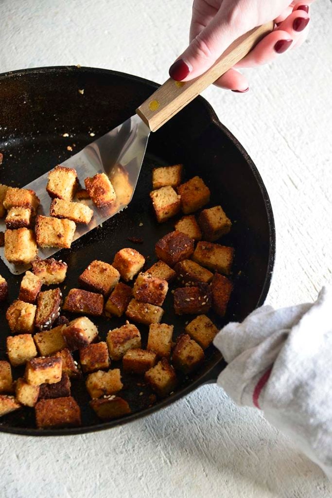 bacon croutons in a cast iron skillet with a wood handled spatula
