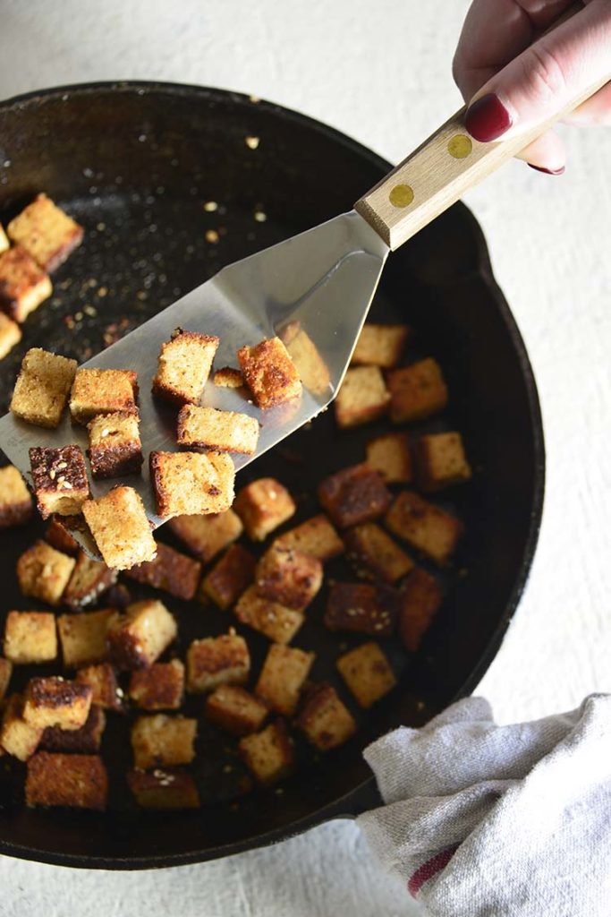 bacon croutons in a cast iron skillet with a wood handled spatula