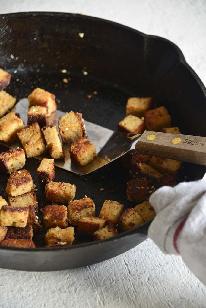 bacon croutons in a cast iron skillet with a wood handled spatula