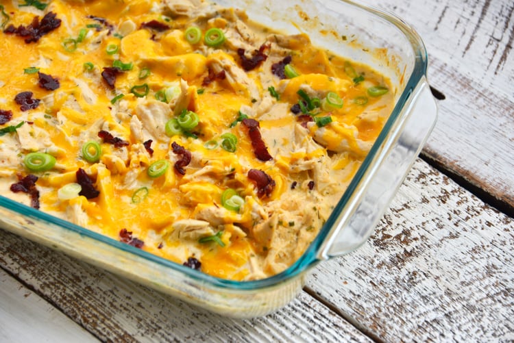 fully baked chicken topped with shredded cheddar cheese, bacon, and scallions in a glass baking dish
