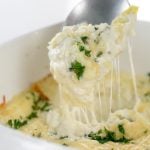 square image of Baked Creamy garlic parmesan hot artichoke dip in a white square casserole dish with a silver spoon taking a scoop