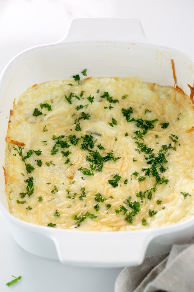 Vertical image of Baked Creamy garlic parmesan hot artichoke dip in a white square casserole dish
