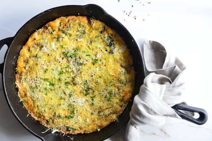 horizontal image of a baked frittata in a cast iron skillet close up with a white fabric napkin
