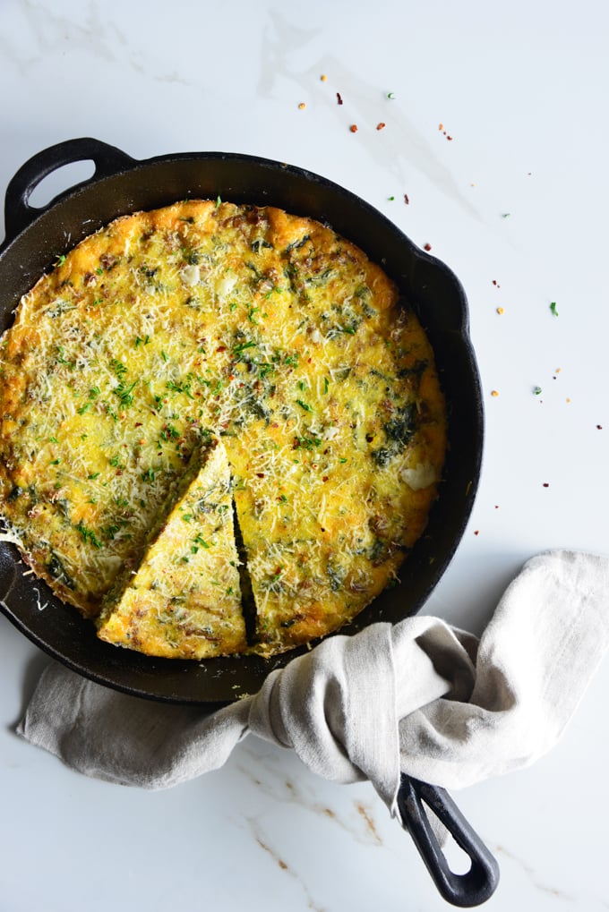 vertical image of a baked frittata in a cast iron skillet close up with a white fabric napkin