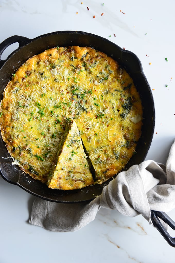 vertical image of a baked frittata in a cast iron skillet close up with a white fabric napkin