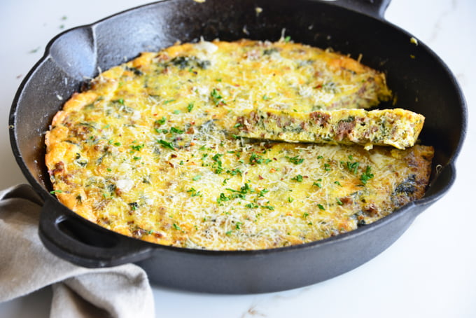 horizontal image of a baked frittata in a cast iron skillet close up with a white fabric napkin
