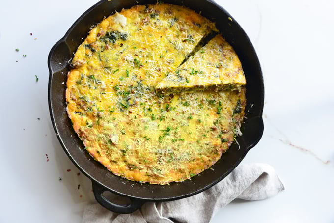 horizontal image of a baked frittata in a cast iron skillet close up with a white fabric napkin