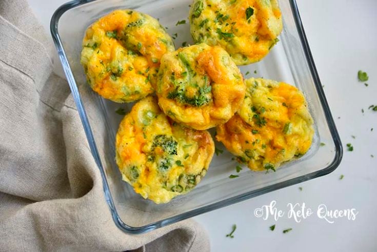 overhead horizontal image of broccoli and cheddar egg muffins in a glass storage container with a napkin