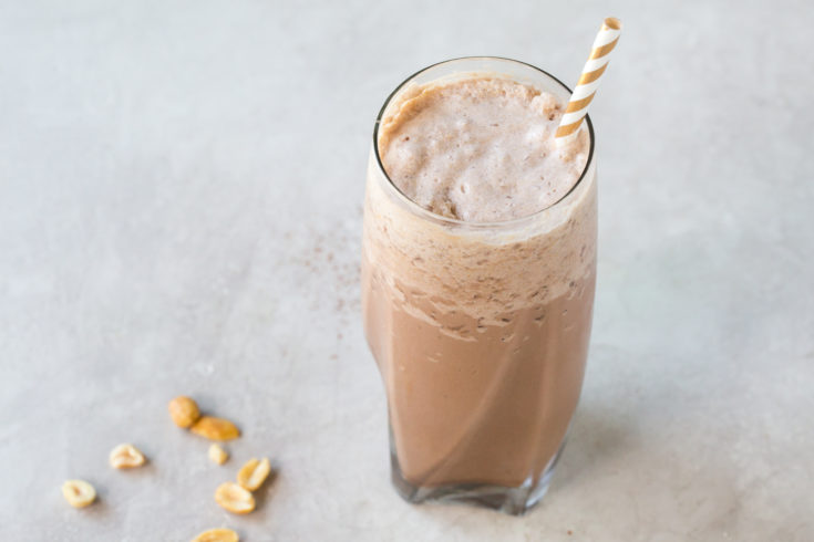 low carb chocolate peanut butter milkshake in a tall glass with a straw on a grey background