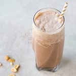 low carb chocolate peanut butter milkshake in a tall glass with a straw on a grey background