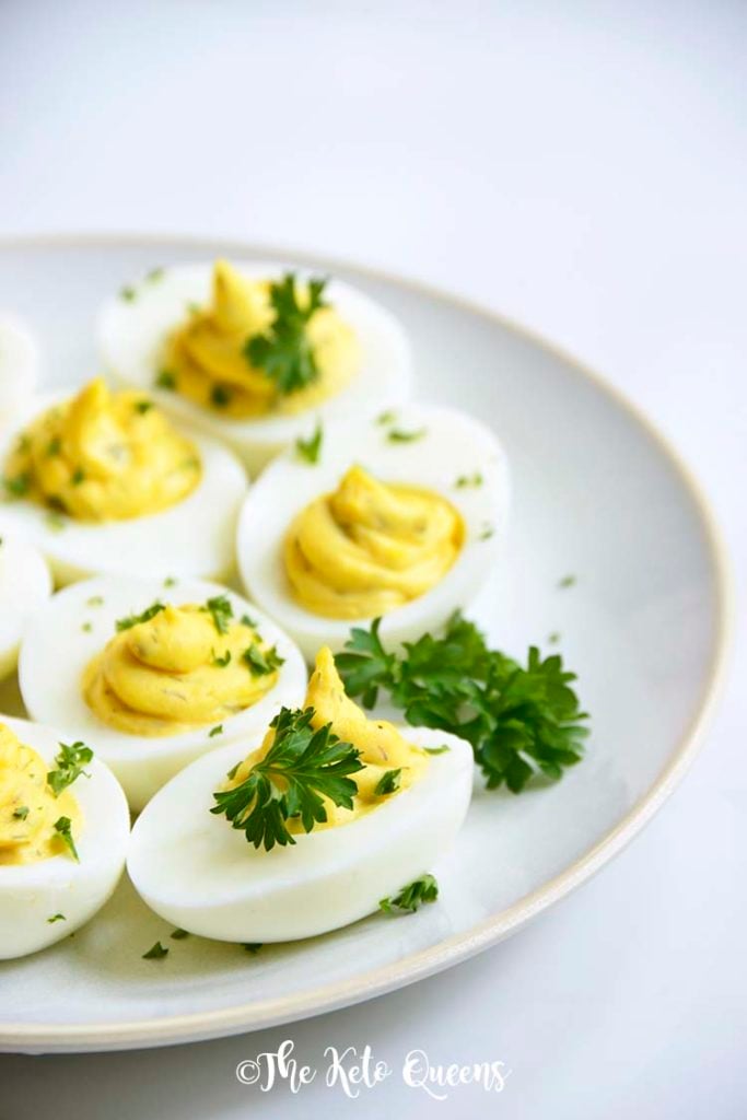 Vertical Image of a bunch of keto Instant Pot Deviled Eggs with Relish on a white plate with a white background with parsley on top made with leftover hard boiled eggs