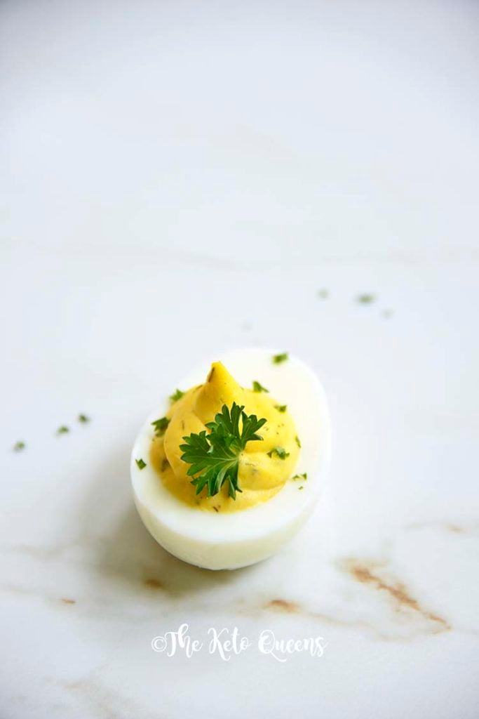 Vertical Image of 1 keto Instant Pot Deviled Eggs with Relish on a white plate with a white background with parsley on top