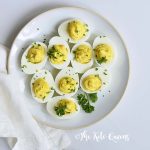 Vertical Image of a bunch of keto Instant Pot Deviled Eggs with Relish on a white plate with a white background with parsley on top