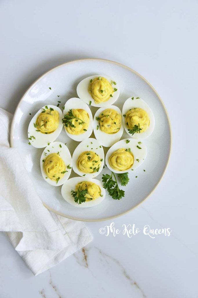 Vertical Image of a bunch of keto Instant Pot Deviled Eggs with Relish on a white plate with a white background with parsley on top made with leftover hard boiled eggs