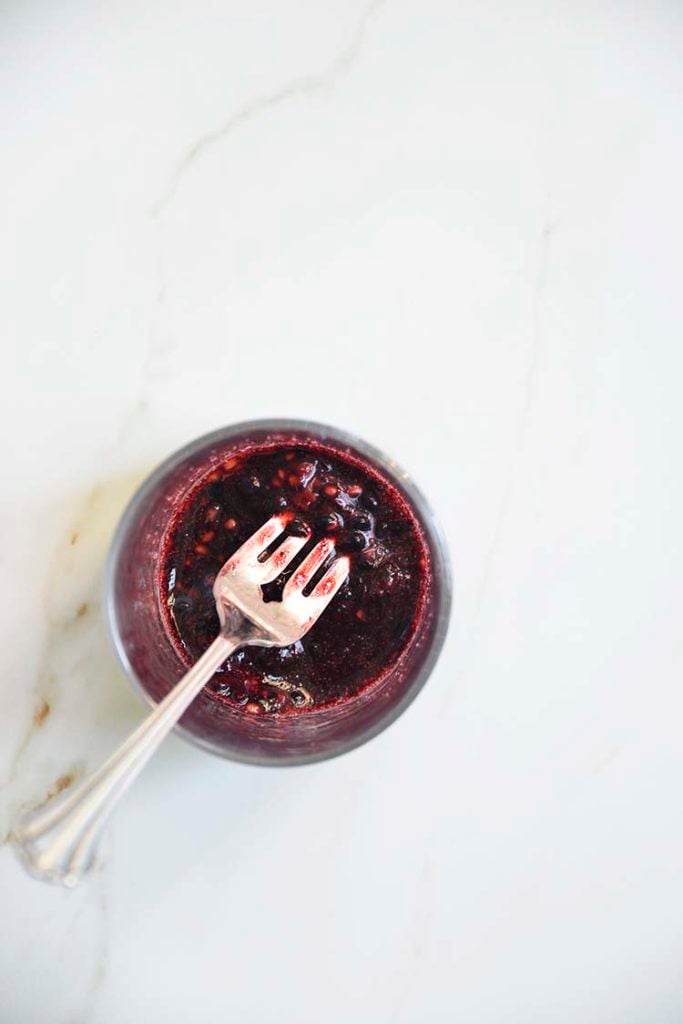 muddled blackberries in a glass with a fork