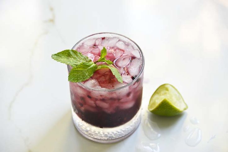 Sparkling Blackberry Bourbon Smash in a clear class topped with mint and lemon wedge on the side