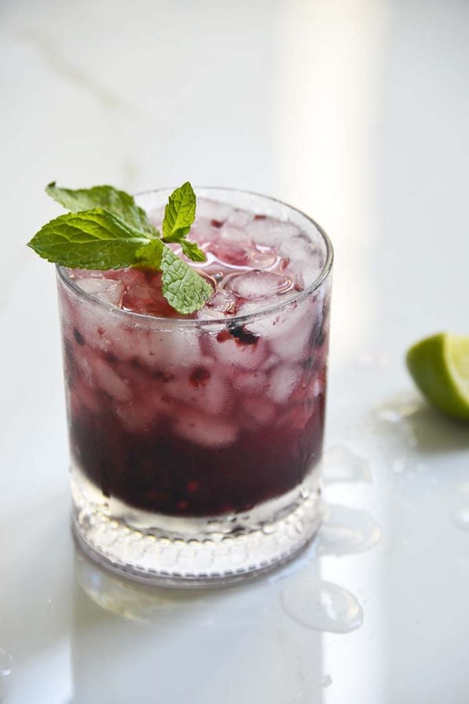 Sparkling Blackberry Bourbon Smash in a clear class topped with mint and lemon wedge on the side