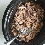 shredded pork in a black slow cooker with 2 forks