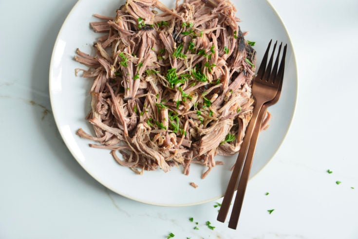 slow cooker pork butt shredded on a white plate with 2 forks