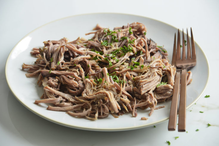 slow cooker pork butt shredded on a white plate with 2 forks