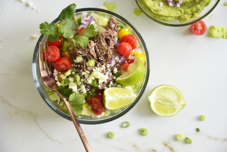 Shredded Beef Keto Taco Salad Recipe in a glass bowl with a fork on a white background with lime