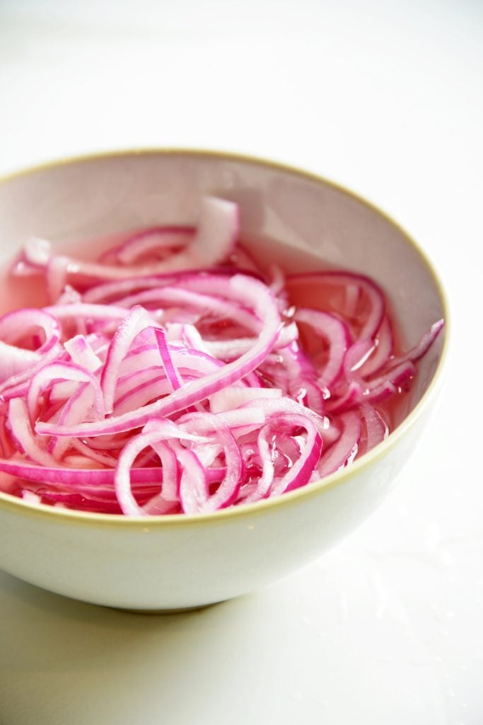 close up of pickled red onions in a white bowl