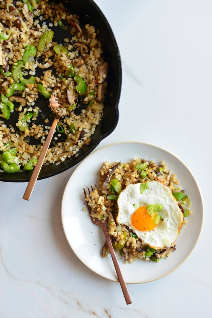 cauliflower fried rice in a cast iron skillet with a spoon and a plate topped with an egg