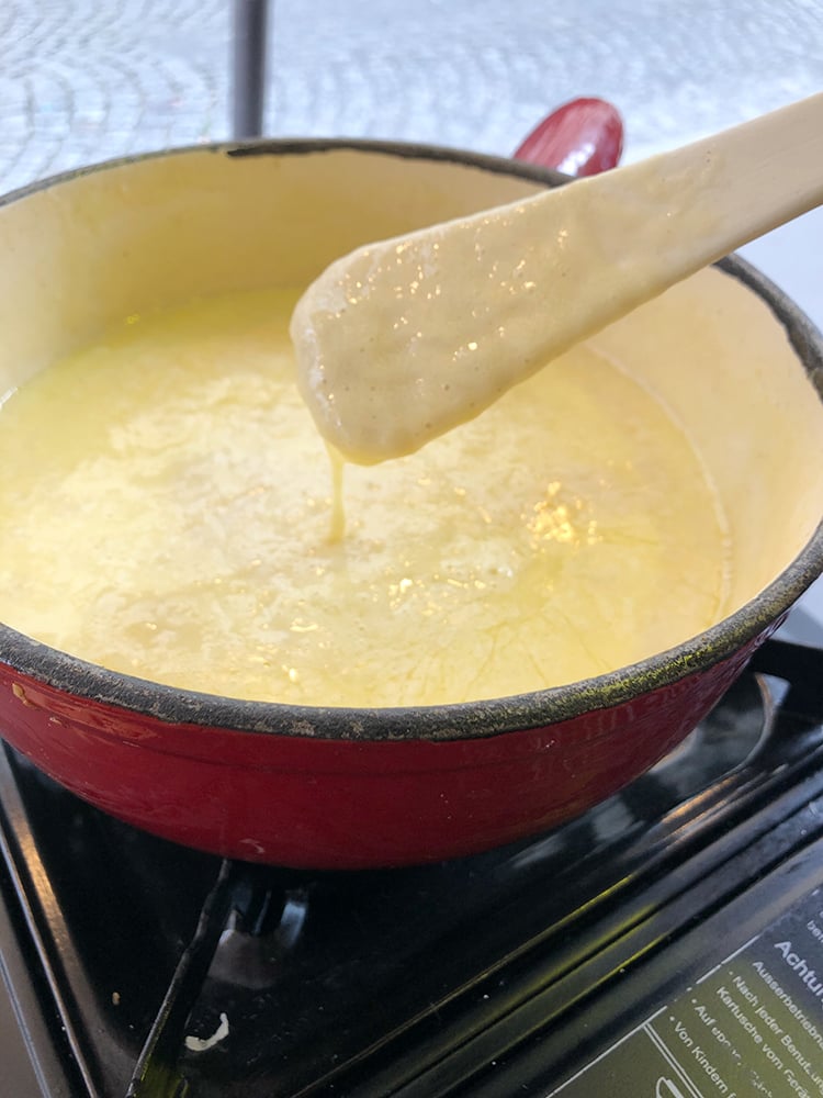 Fondue Dripping Off White Spoon Into Red Pot