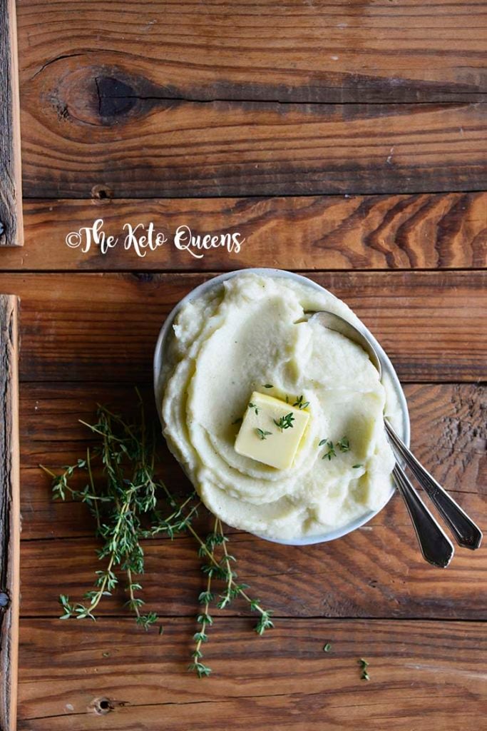 Pinterst image for low carb butter garlic mashed cauliflower Vertical image from above of mashed cauliflower with fresh thyme and butter in a bowl with 2 spoons
