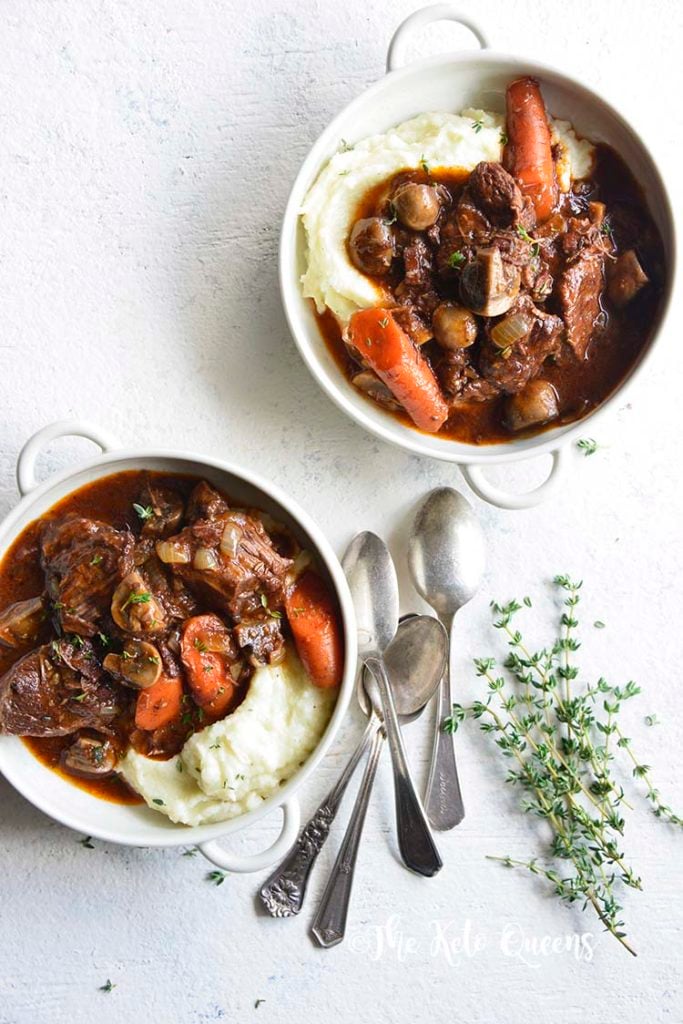 vertical image of 2 low carb instant pot beef stew in a white bowl with 3 spoons and fresh herbs on a white background