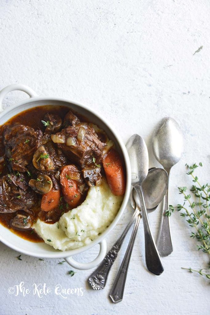 vertical image of low carb instant pot beef stew in a white bowl with 3 spoons and fresh herbs on a white background