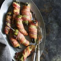 Keto Bacon-Wrapped Cheese-Stuffed Jalapeno Poppers on a silver tray with forks on a dark background