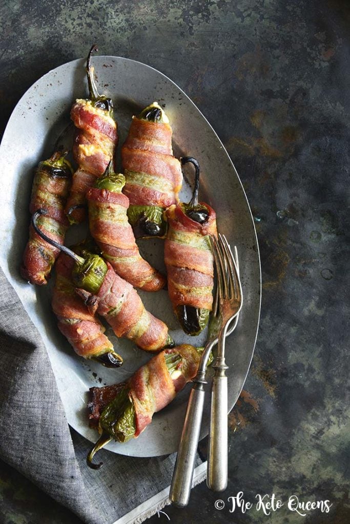 Keto Bacon-Wrapped Cheese-Stuffed Jalapeno Poppers on a silver tray with forks on a dark background