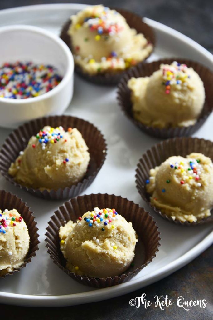 vertical image of keto breakfast meal prep of keto sugar cookies fat bombs on a silver platter with sprinkles in a brown wrapper