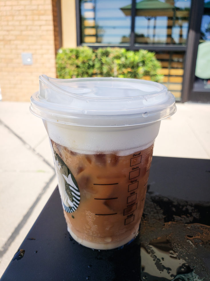 Tired of boring black coffee? Check out my top 5 Keto Starbucks Drinks to brighten your morning. image of a Iced Starbucks Blonde Cold Foam Cappuccino on a table outside of starbucks