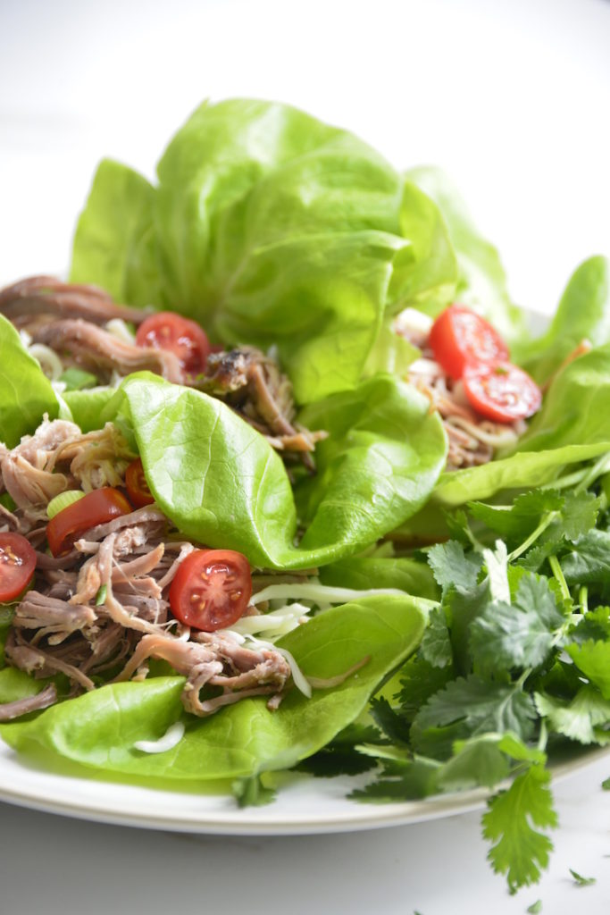 Lettuce Wrapped Leftover Pulled Pork Tacos topped with cheese and tomatoes on a white plate