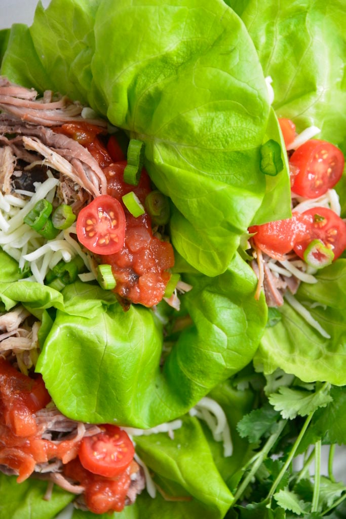 Lettuce Wrapped Leftover Pulled Pork Tacos topped with cheese and tomatoes on a white plate