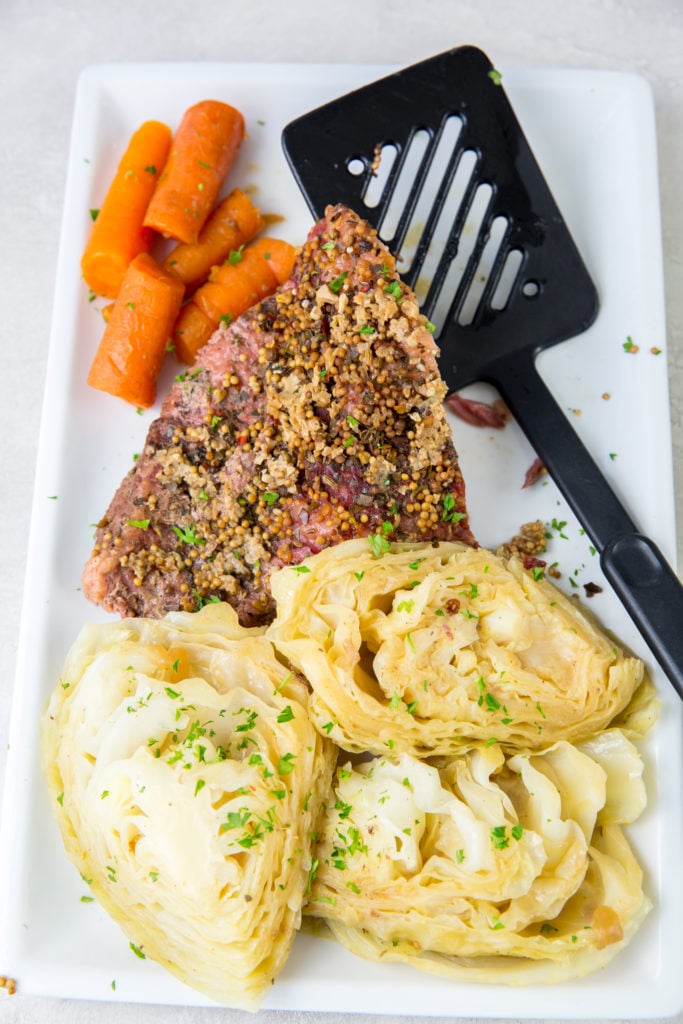vertical image of corned beef, cabbage and carrots on a white plate with a spatula