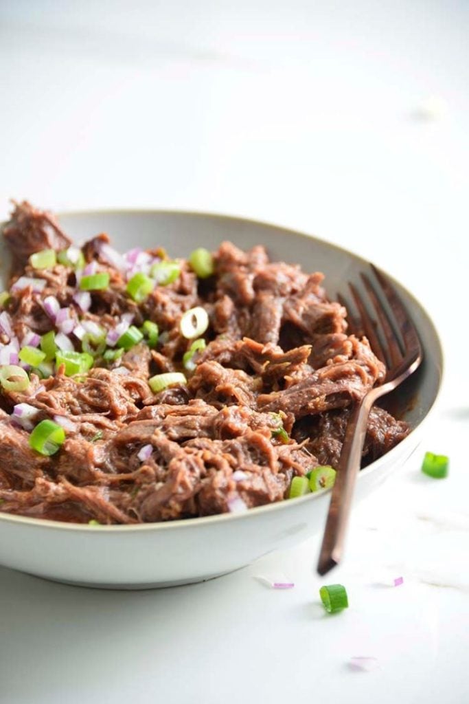 low carb pulled bbq beef recipe in a bowl with a fork on a white background