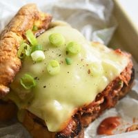 Keto BBQ Pulled Pork Sandwich on parchment paper with scallions and pickles