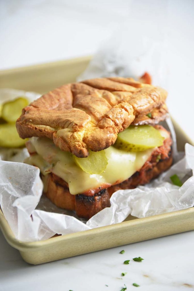 Keto BBQ Pulled Pork Sandwich on parchment paper with scallions and pickles