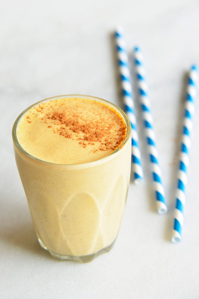 keto pumpkin smoothie in a clear glass with blue striped straws