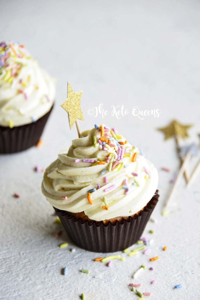 vertical image of a keto cupcake - vanilla cupcake with white chocolate buttercream frosting with sprinkles and a star
