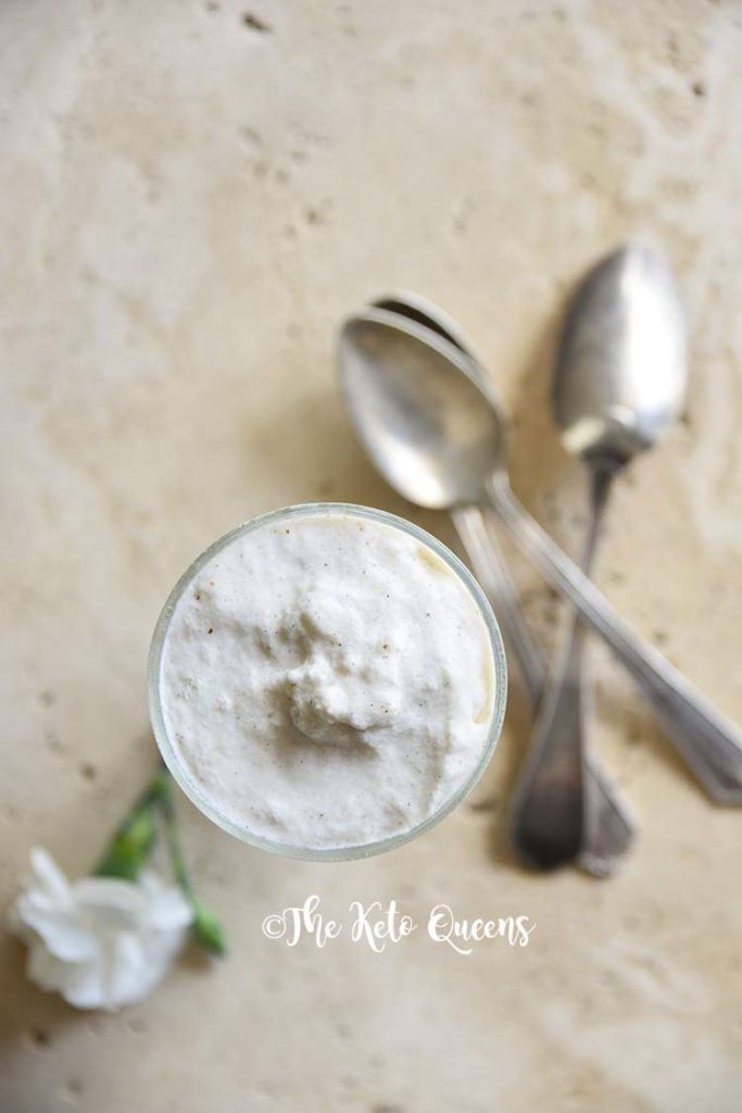 homemade vanilla bean keto milkshake in a tall glass with spoons and white flowers
