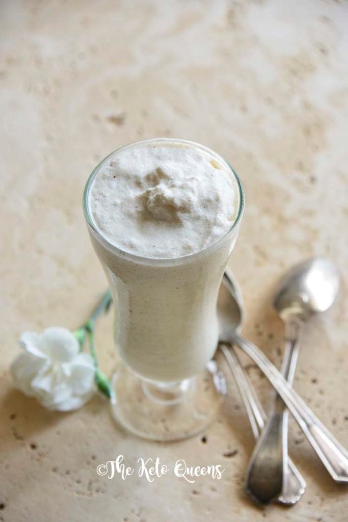 homemade vanilla bean keto milkshake in a tall glass with spoons and white flowers
