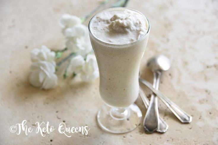 homemade vanilla bean keto milkshake in a tall glass with spoons and white flowers